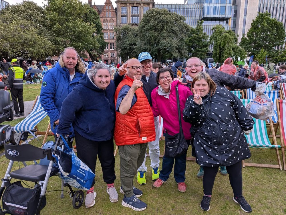 Seven get2gether members standing together on the grass at an outdoor event in Edinburgh, smiling at the camera, some giving a thumbs up and a peace sign