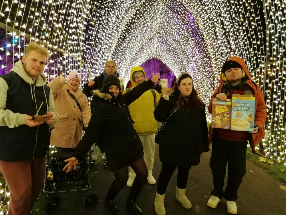 A group of members laughing under a tunnel of golden fairy lights on a night out