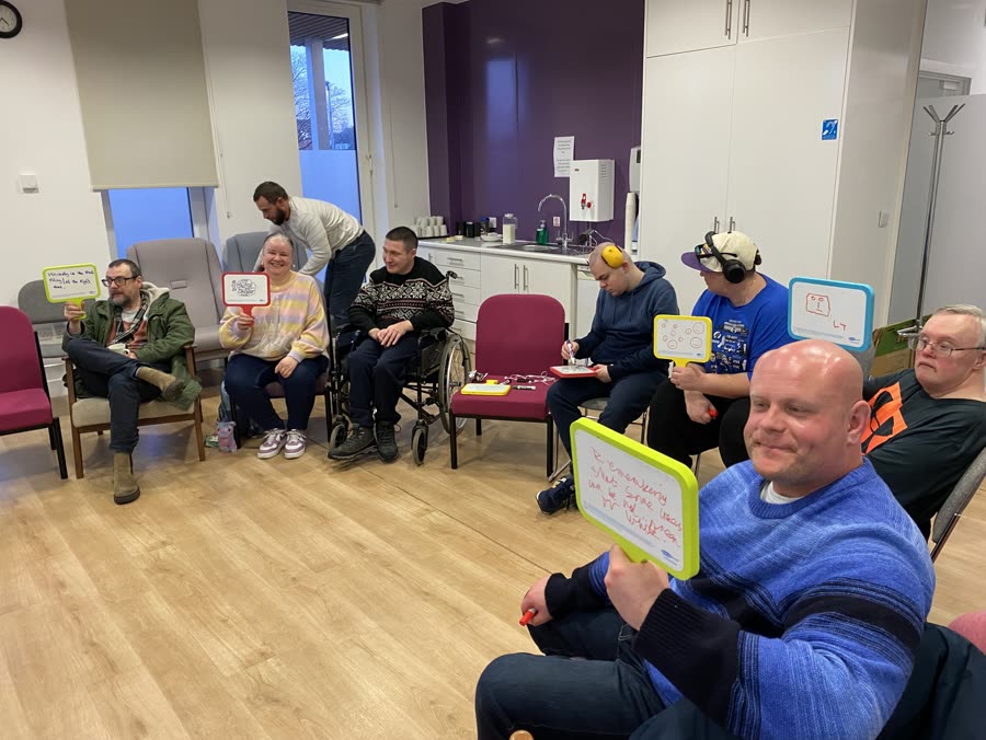 Members in a workshop circle holding up whiteboards with their answers