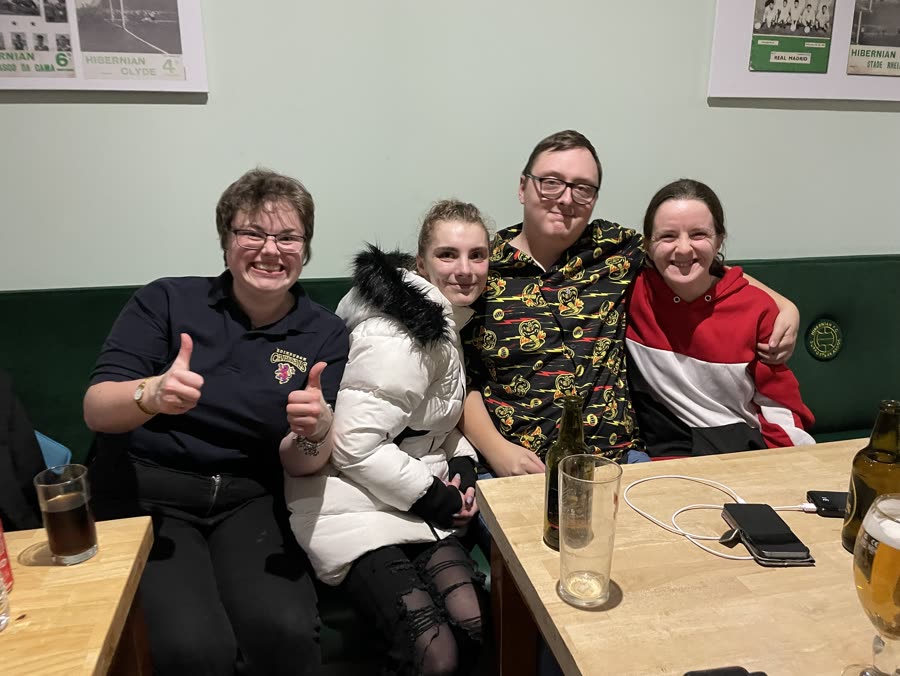 Four friends sitting together at a pub table, one giving a double thumbs up