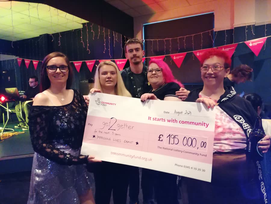Five smiling members holding a giant National Lottery Community Fund cheque for £195,000