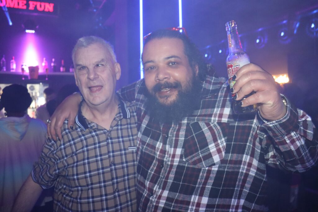 Member Scott has his arm around another member, both are smiling. Scott is holding a drink. 